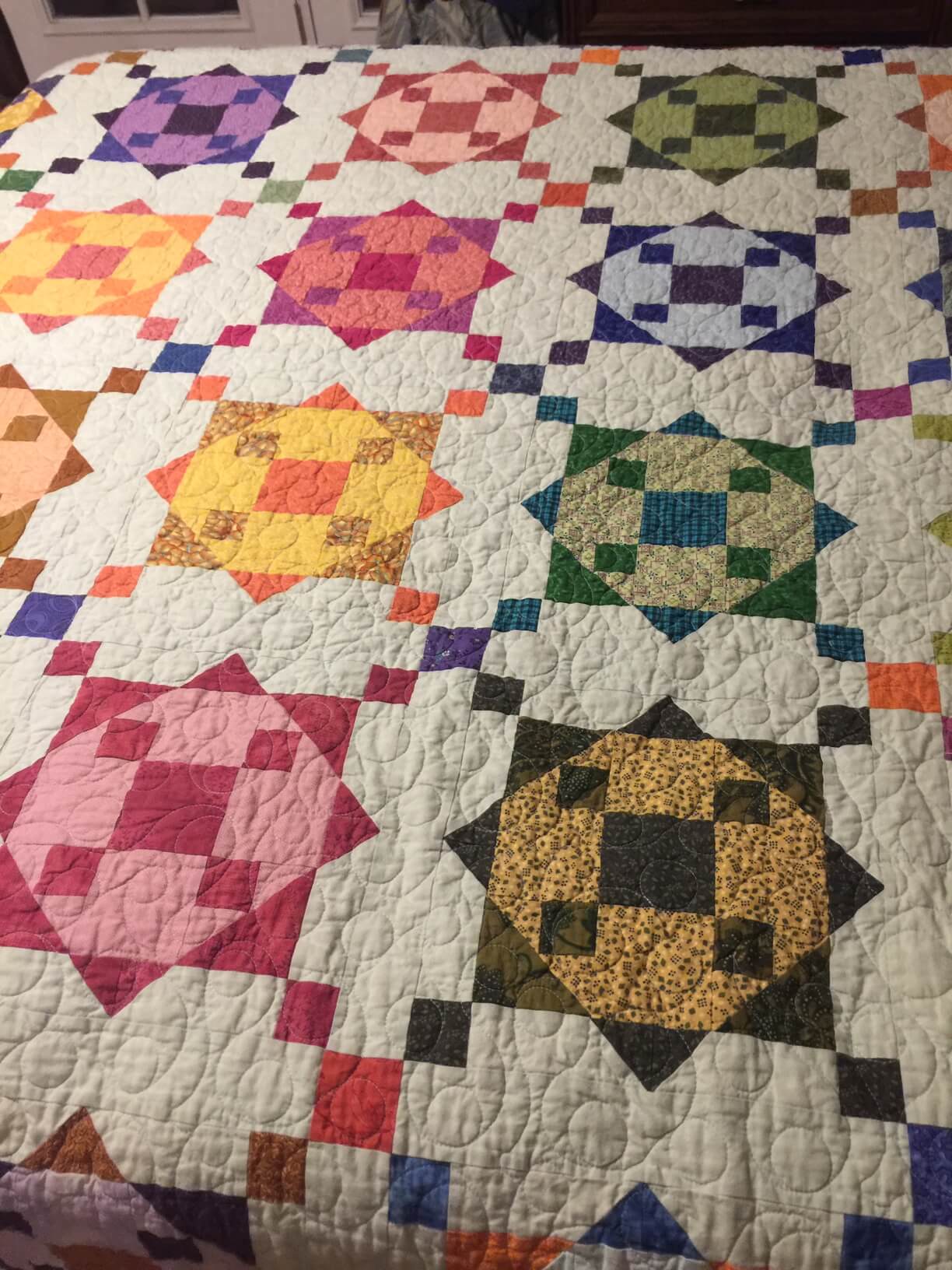 Quilt of multicolored star blocks on a stitched white background