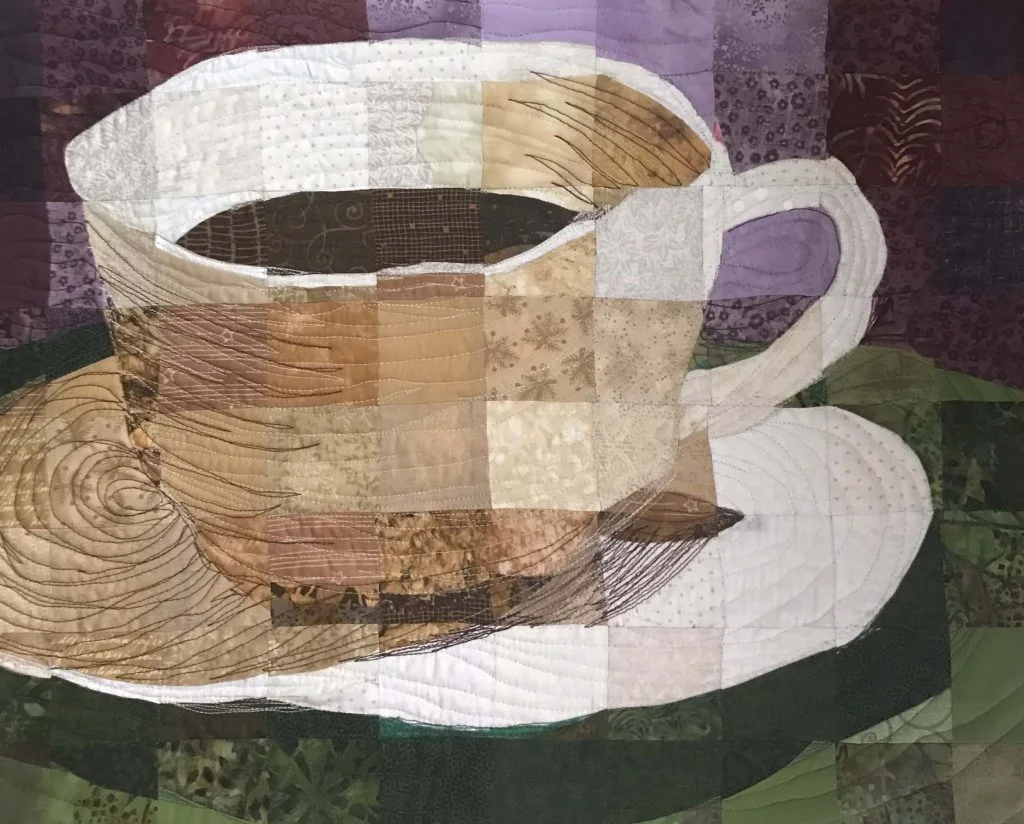Art quilt showing a cup of coffee on a saucer, pieced from small fabric squares