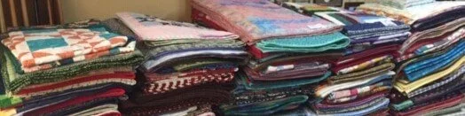 Tall stacks of folded quilts in many colours standing side by side on a table