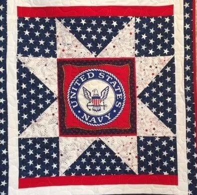 A veterans' quilt with an eight-pointed star of off-white and navy triangles around a United States Navy emblem on a red ground